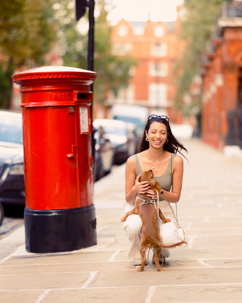 A woman kneels down to greet her dog. Next to them is a large red postbox.